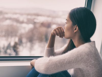 Winter depression - seasonal affective disorder mental health woman sad comtemplative looking out the window alone.